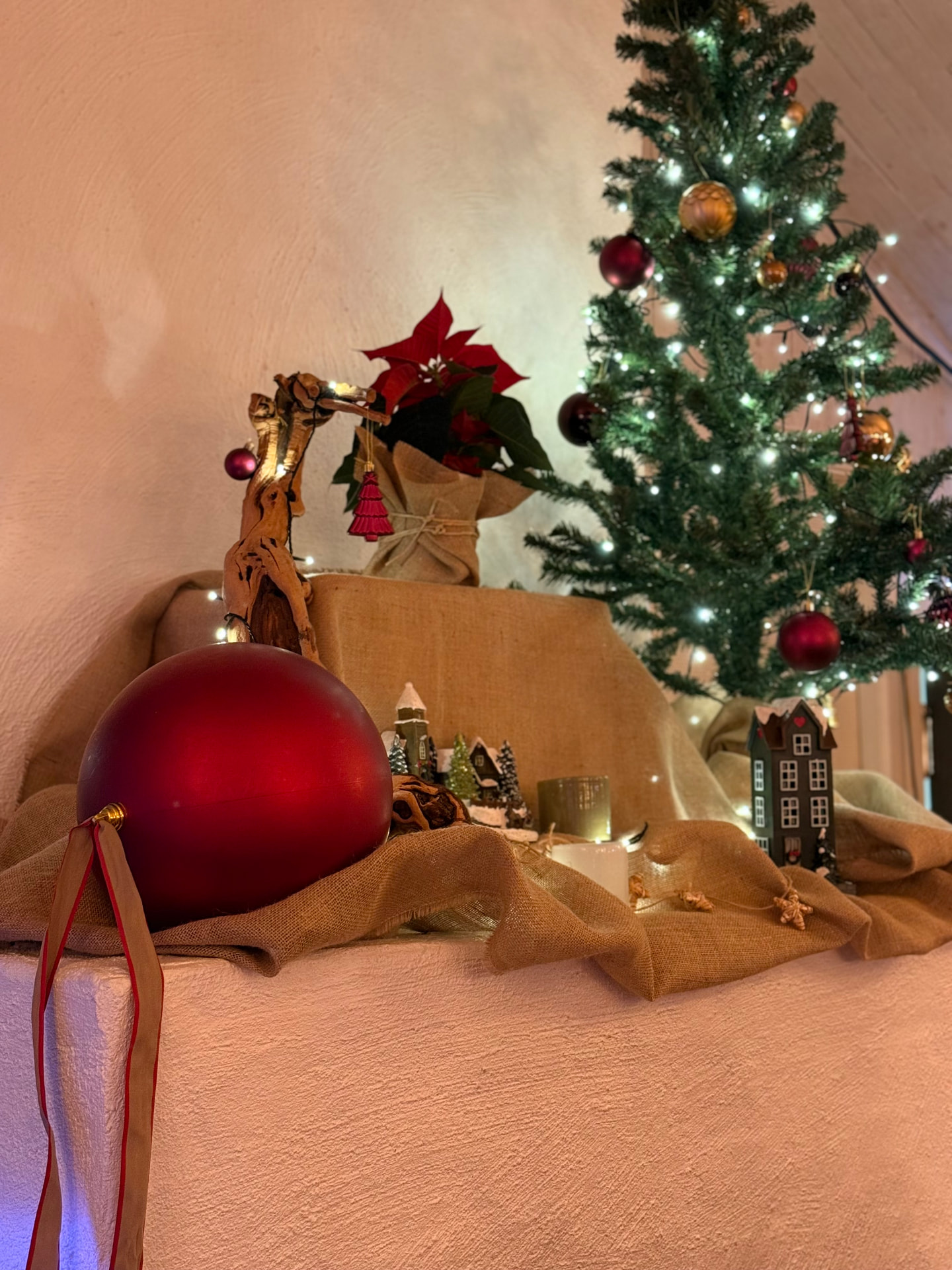 Juldekoration med stor röd kula, stjärnblomma och gran på en vitmålad spis